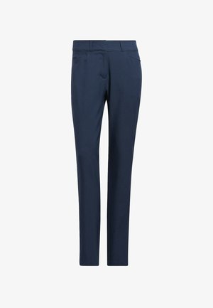 Frau geht, trägt ein weißes Kurzarm-Poloshirt, marineblaue Hose und weiße Sneaker vor einfachem Hintergrund.