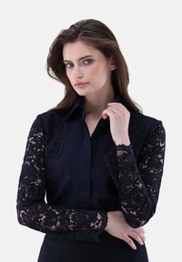 Marinebluse mit langen Spitzenärmeln im floralen Muster, einem klassischen Kragen und Knopfverschluss. Glatte Stoff mit strukturierten Spitzelementen.