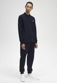 Tumes sinine pika varrukaga polo särk krae ja väikese valge logoga. Kombineeritud sobivate tumesiniste dressipükste ja valgete spordijalatsitega. Sile tekstuur.