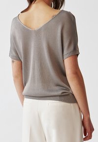 Maglia grigia a maglia presenta un retro a scollo a V e maniche corte, con dettagli a coste sul collo e sull'orlo. Abbinata a pantaloni di colore chiaro.