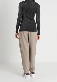 Haut à col roulé noir pailleté, ajusté avec des manches longues, associé à un pantalon beige à rayures et des baskets blanches avec des accents violets.