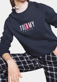 Námořnická mikina s vyšitým logem "TOMMY JEANS" v bílé a červené barvě. Disponuje žebrovanými manžetami a spodním lemem, doplněná o kalhoty v černobílé kostce.