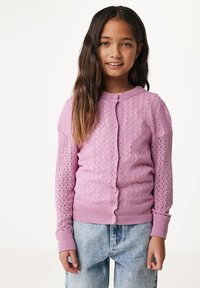 Ljusrosa stickad cardigan med diamantmönster, rund hals och knappstängning. Ribbad mudd och nederkant, bärs över blå denimjeans.