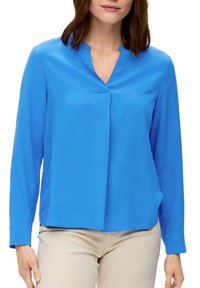 Blouse bleue à manches longues avec un décolleté en V, présentant une texture légère et lisse ainsi qu'un devant plissé. Le design est de coupe décontractée.