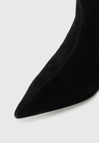 Stivale alla caviglia in suede nero con punta affusolata, texture liscia e dettagli di cuciture sottili lungo le cuciture.