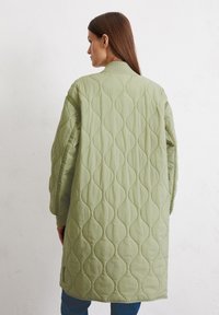 Gevoerde lange jas in lichtgroen, met een geribde kraag, een oversized pasvorm en een golvend gestikt patroon op de rug. Zachte textuur.