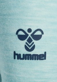 Ljusblått tyg med en texturerad yta, som har en mörkblå logotyp och varumärkesnamnet "hummel" under. Designen är enkel och tydlig.