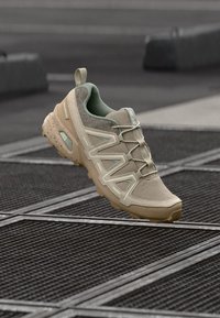 Fica dado o sapatilha desportiva bege com materiais de malha e camurça, acentos texturizados, sola de borracha e um design em camadas proeminente.