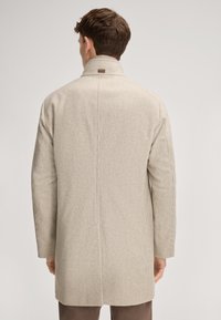 Beige houndstooth-gepatroneerde jas met hoge kraag en rechte snit, voorzien van lange mouwen en een logotag aan de achterkant.