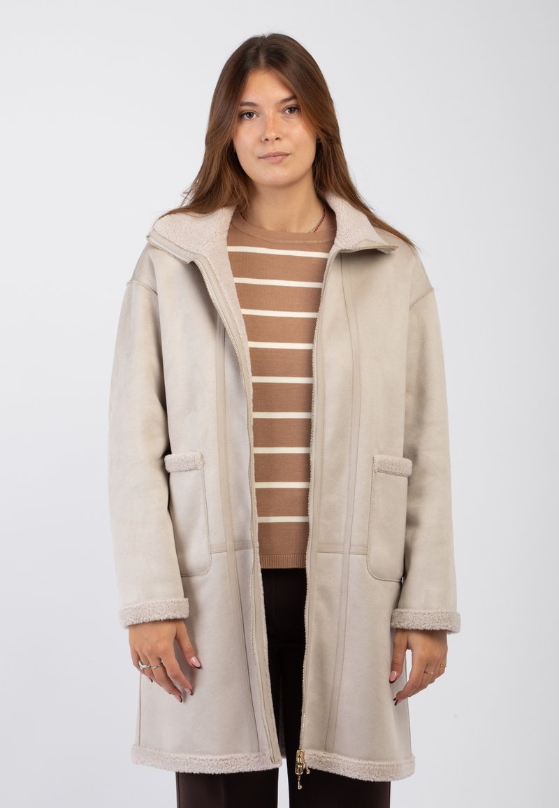 Cappotto in finta suede beige con zip frontale, tasche laterali e rifiniture morbide e texturizzate. Presenta un collo alto e un design a lunghezza media.