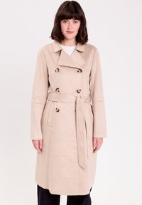 Cappotto trench beige realizzato in tessuto morbido, con design doppiopetto, bottoni in resina tartaruga e cintura annodata in vita.