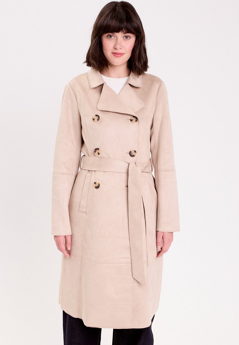 Cappotto trench beige realizzato in tessuto morbido, con design doppiopetto, bottoni in resina tartaruga e cintura annodata in vita.