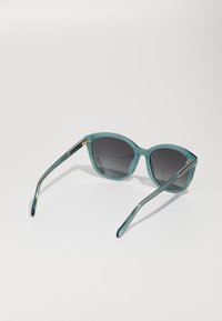 Een paar acqua-kleurige, oversized zonnebrillen met donkere gradient lenzen en efficiënte, gebogen armen met subtiele gouden accenten.