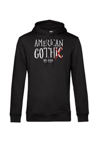 Felpa nera realizzata in tessuto morbido, con un audace testo grafico bianco "AMERICAN GOTHIC" dove la parola "GOTH" è barrata in rosso, e "WEDNESDAY" sotto.