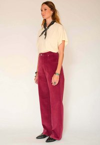 Pantalons en velours côtelé taille haute bordeaux, associés à un t-shirt jaune clair et un bandana noir. Les chaussures ont des pointes aiguës avec des clous.