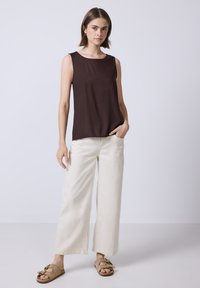 Haut sans manches marron avec encolure ronde, associé à un pantalon large crème et des sandales beiges à enfiler avec un nœud.