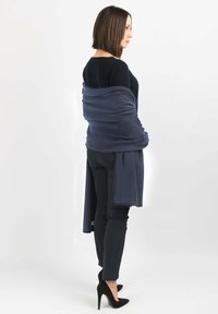 Shawl avvolgente navy drappeggiato sulle spalle, realizzato in tessuto morbido, con una texture liscia e estremità allungate. Abbinato a pantaloni neri aderenti.