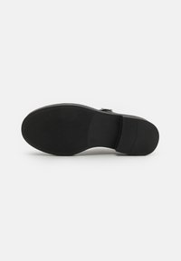 Black shoe sole with textured surface, featuring a smooth section and slight heel. Includes a circular logo detail near the arch.