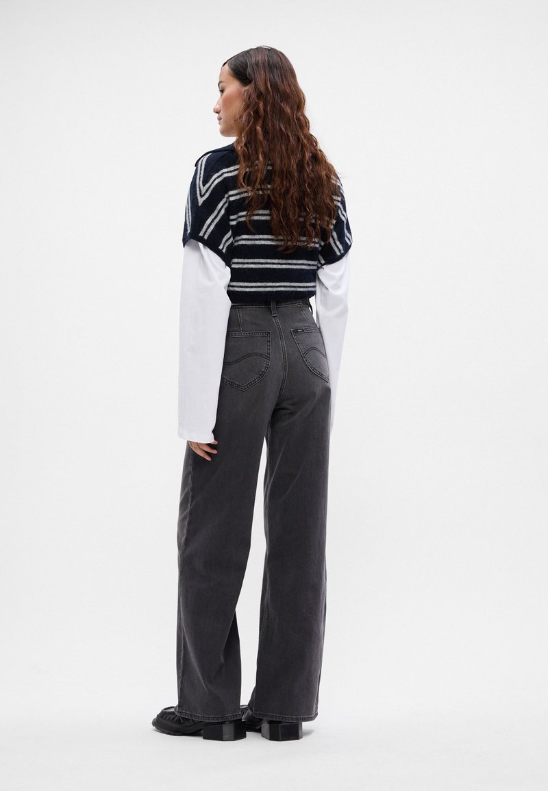 Przycięty granatowy sweter w paski na białej koszuli z długim rękawem, zestawiony z szarymi spodniami typu wide-leg z wysokim stanem i masywnymi czarnymi botkami.