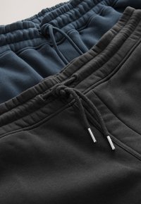 Dve pari trenirk v mornarsko modri in črni barvi. Obe imata elastičen pas z vezalkami in kovinskimi nasadki, narejeni iz mehke tkanine.