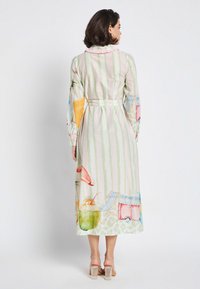 Langes Kleid mit Pastellmuster in grünen Streifen, das farbenfrohe Obst- und Strandmotive zeigt, mit einem Gürtel in der Taille und Rüschendetails am Kragen.