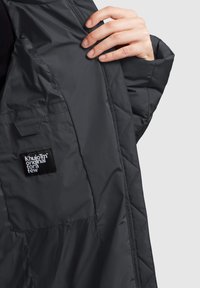 Kvdeldatud must jakk, millel on siledast ja läikivast materjalist välispind. Omab plaastriga silti ja diagonaalset õmblusdisaini. Käega paigutatud kangale.