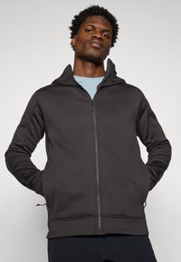 Felpa nera con zip e colletto alto, dotata di un logo discreto. Realizzata in un tessuto morbido e elasticizzato, presenta un design aderente e tasche laterali.