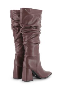 Par de botas altas, holgadas, de cuero marrón oscuro, con tacones cuadrados y un pequeño logo metálico cerca del borde superior.