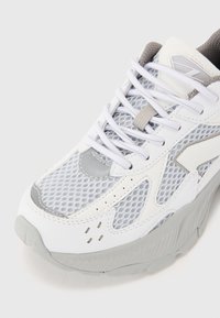 White and gray athletic shoe featuring mesh panels, rubber sole, and lace-up design with reinforced toe and subtle detailing on sides.