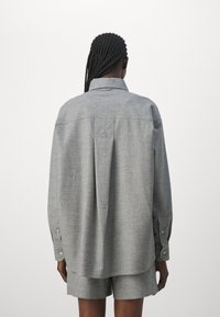 Chemise grise surdimensionnée avec un col boutonné, des manches longues et un ourlet droit. Dispose d'un pli au dos et d'une texture de tissu lisse.