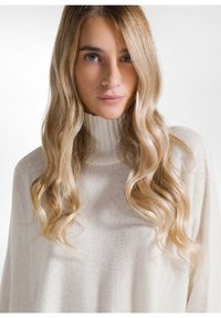 Ivory turtleneck sweater gemaakt van zacht, textuurmateriaal. Heeft een geribbelde halslijn en een relaxte pasvorm. Lang, golvend haar dat het gezicht omlijst.