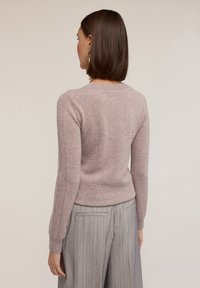 Morbido maglione rosa chiaro con collo a giro e dettagli a coste sulle maniche, abbinato a pantaloni grigi a righe.