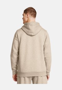 Beige hoodie med en blød tekstur, der har snoretræk i hætten, lange ærmer og ribbet kant, båret afslappet set bagfra.