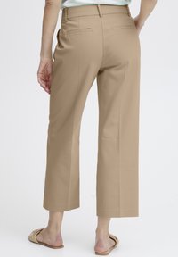 Pantalons beige à jambes larges, tissu lisse, taille mi-haute, deux poches arrière, devant plat, design ajusté, associés à des sandales à glissière neutres.