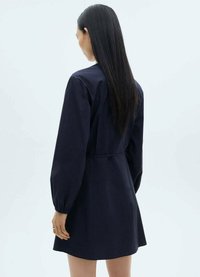 Rochie din bumbac de culoare albastru marin, cu manșete lungi tip balon, talie ajustată și fustă evazată. Textură netedă, design simplu. Vedere din spate.