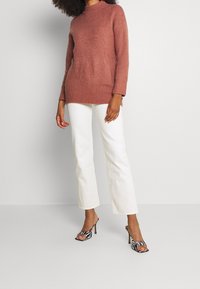 Rosa stickad tröja med hög krage, kombinerad med vita flare byxor och svart-vit randiga högklackade skor.