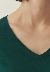 Pull vert en tricot avec un col en V. Gros plan montrant la texture fine et les détails de couture au niveau de l'encolure et du col.