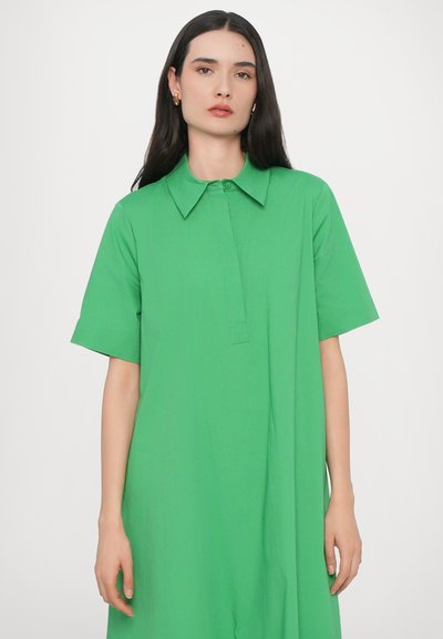 Zielona krótko rękawowa sukienka z ostro zakończonym kołnierzykiem, zapięciem na guziki i luźnym krojem. Wykonana z gładkiego, lekkiego materiału.