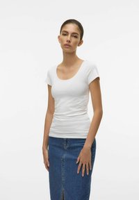 T-shirt bianco aderente a maniche corte con scollatura a girocollo, abbinato a una gonna di jeans di lunghezza media con uno spacco frontale.