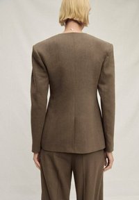 Rjav elegantni blazer z oblikovanimi rameni in enim zadajšnjim razporkom. Izdelan iz teksturirane tkanine. Obut z ujemajočimi hlačami.