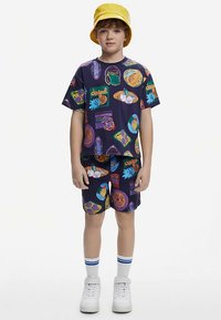 Purple short-sleeve t-shirt and shorts, featuring colorful patterns and graphics. Paired with white sneakers and a yellow bucket hat.