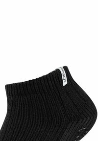 Calza nera lavorata a maglia, con texture a costine e un'etichetta bianca. Presenta una vestibilità aderente e una forma curvata vicino alla caviglia.