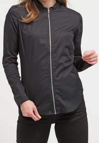 Svart lättviktsjacka med hög krage, fullständig dragkedja fram, långa ärmar och rundad fåll, tillverkad av slätt, glänsande tyg.