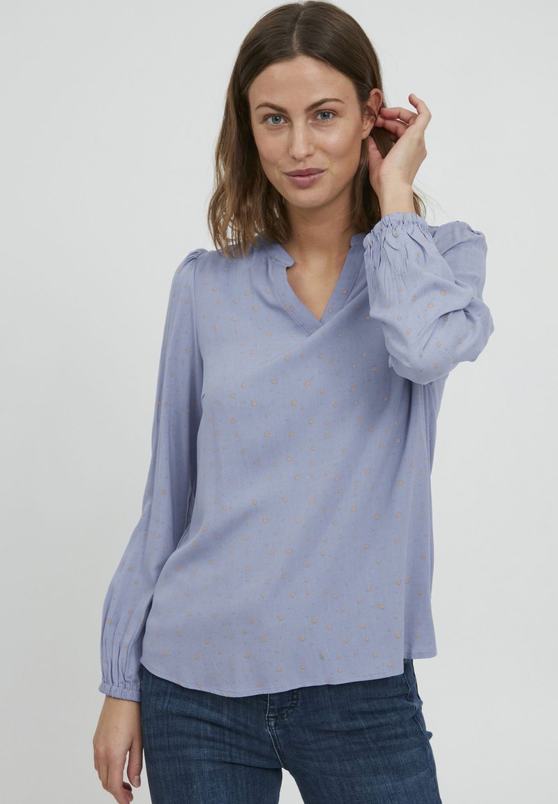 Blusa azzurro chiaro con scollo a V, maniche lunghe a sbuffo e piccoli pois beige. Realizzata in un tessuto morbido e liscio.