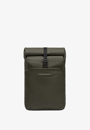 Sac à dos à rabat en vert olive, fabriqué à partir de matériau imperméable. Il dispose d'une sangle noire avec une boucle et d'une poche avant avec un accent argenté.