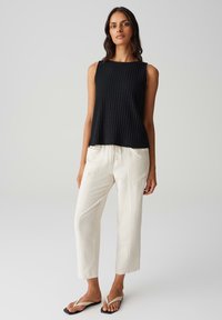 Top nero a coste senza maniche con scollatura rotonda, abbinato a pantaloni bianchi leggeri con cordino in vita e sandali neri piatti.
