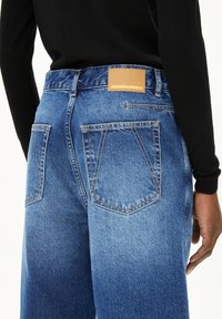 Blauwe denimjeans met een vervaagd ontwerp, voorzien van twee achterzakken, contrasterende stiksels en een bruin merklabel op de tailleband.