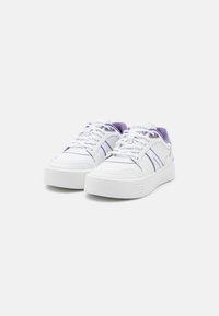White sneakers with purple accents, made of smooth synthetic material, featuring a lace-up design and a thick sole with minimal grooves.