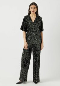 Tuta intera nera con paillettes, maniche corte, scollo a V, vestibilità rilassata e gambe larghe. Presenta paillettes lucenti e testurizzate su tutta la superficie.