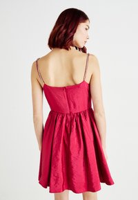 Κόκκινο αμάνικο φόρεμα με εφαρ�μοστό κορσέ και φουσκωτό φουστάνι. Υφασμάτινη επιφάνεια, λεπτές τιράντες με κοσμήματα από χάντρες και διακριτικός κρυφός φερμουάρ στην πλάτη.